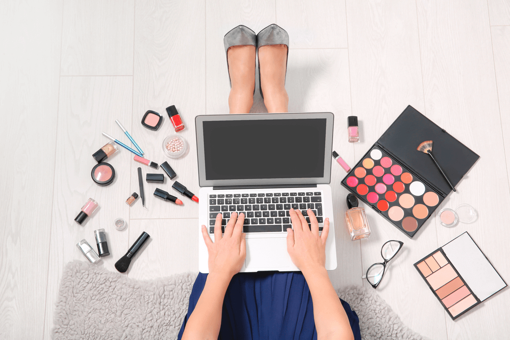 Woman typing on laptop surrounded by makeup