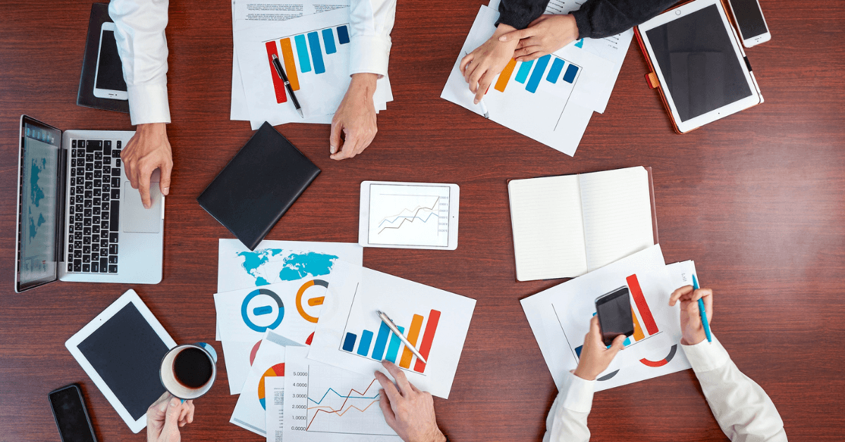 Team of business individuals working together at a table, focused on graphs and papers for a guide on data analytics in clinics.